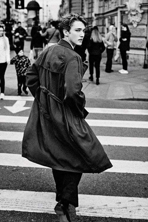 black and white photograph of a woman walking down the street with her coat over her shoulders