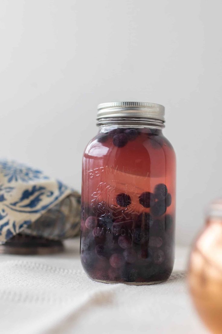 a jar filled with blueberries sitting on top of a table next to a tea bag