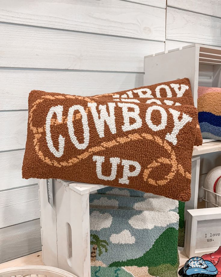 a cowboy up pillow sitting on top of a chair next to other pillows and blankets