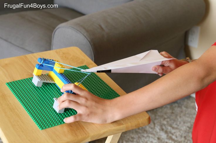 a woman cutting paper on top of a table with legos in front of her