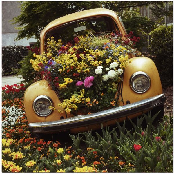 an old yellow car with flowers growing out of it