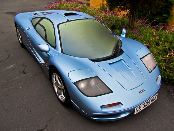 a blue sports car is parked on the side of the road next to some bushes