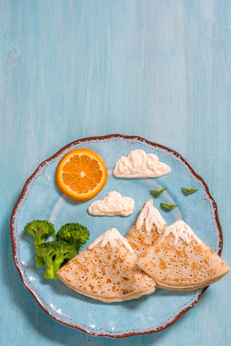 a blue plate topped with food on top of a wooden table next to an orange and broccoli