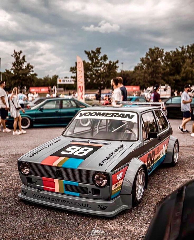 an old race car parked in a parking lot with people walking around it and onlookers