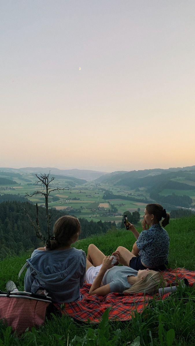 two women sitting on a blanket in the grass with a view of rolling hills and valleys