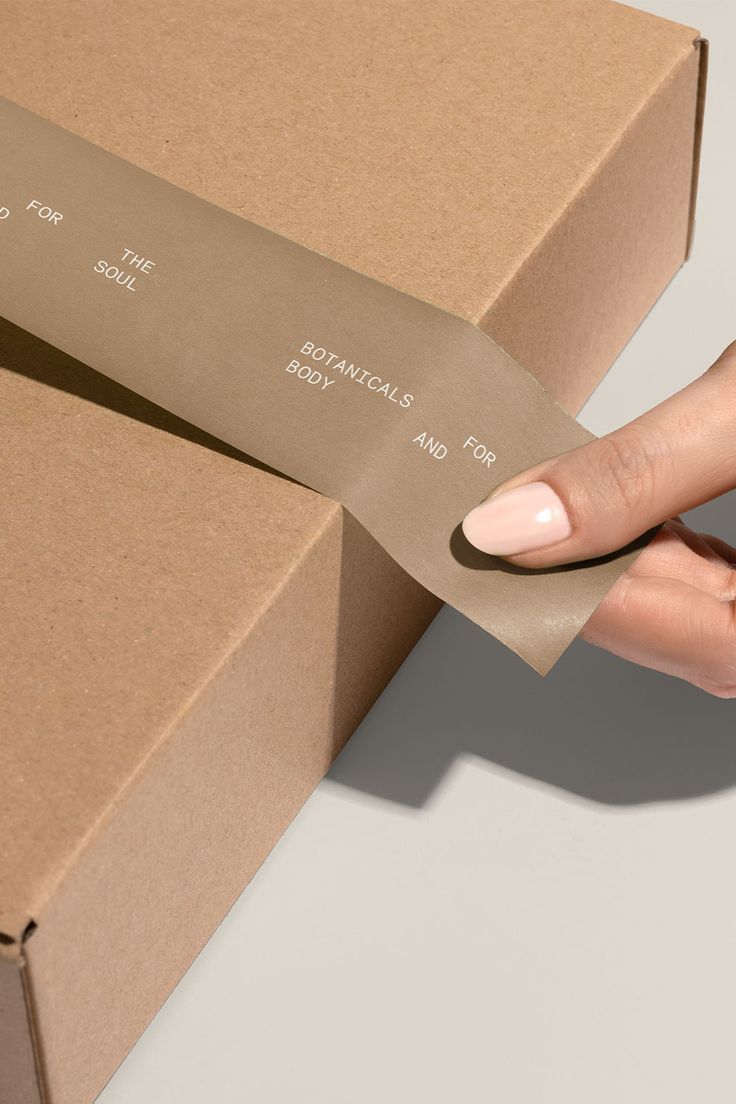 a woman's hand holding a piece of brown paper over a cardboard box that says,