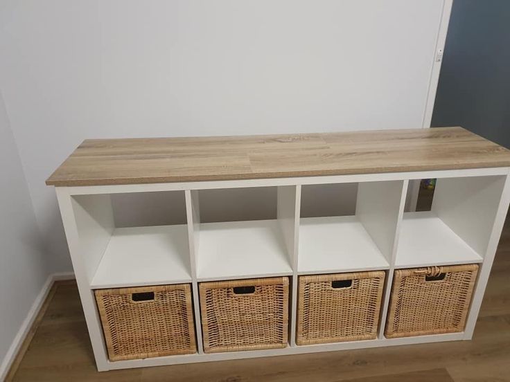 a white shelf with four wicker baskets on top and two wooden shelves above it