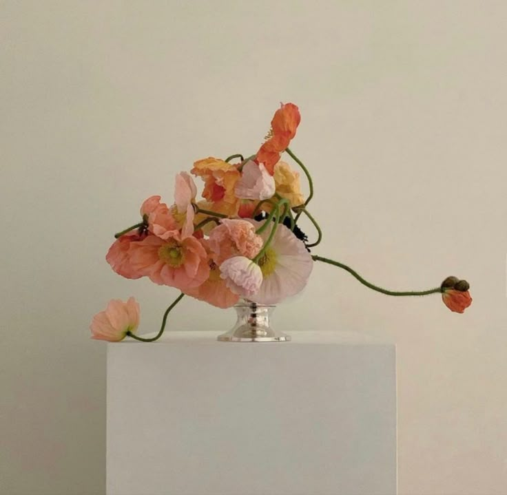 an arrangement of flowers in a vase on a white pedestal against a plain wall background