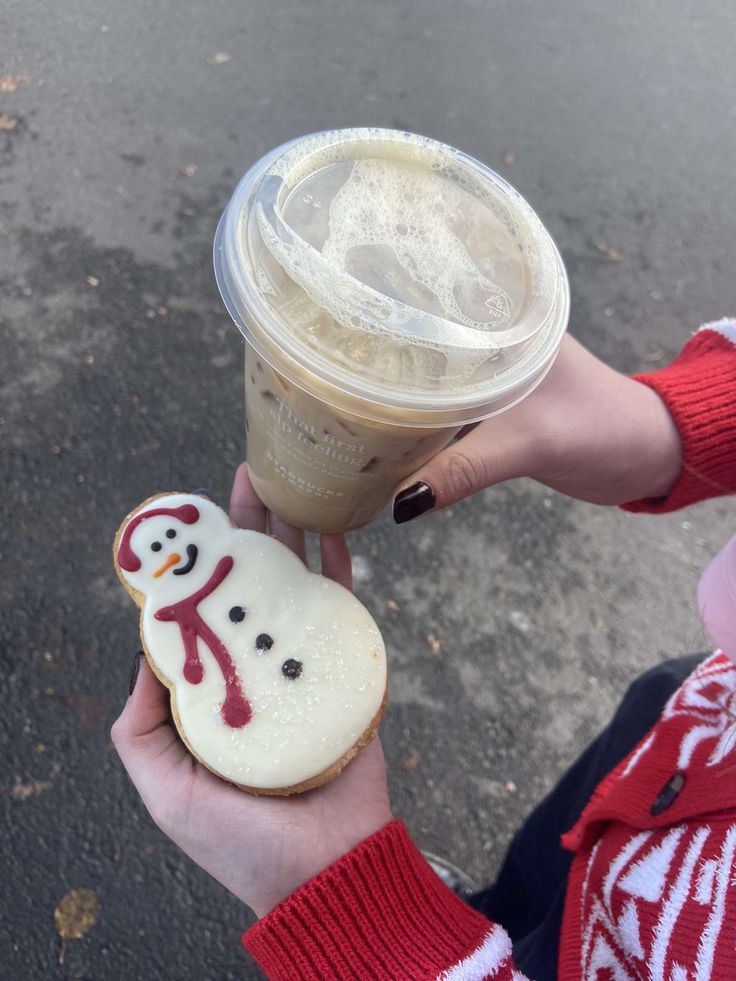 a person holding up a cup of coffee and some cookies with frosting on them