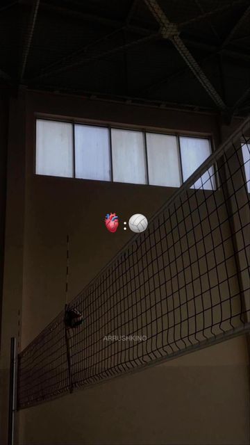 three balls are in the air above a volleyball net inside an indoor gym area with windows