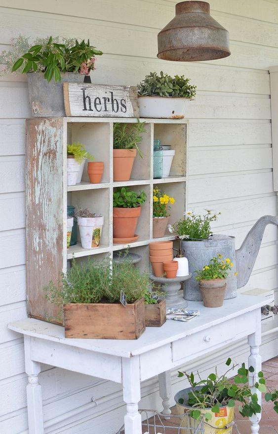 a white table topped with potted plants next to a wooden shelf filled with flowers