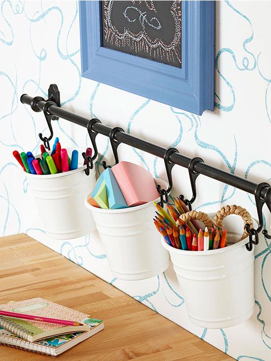 three white buckets filled with pencils and markers on a wooden table next to a blue frame