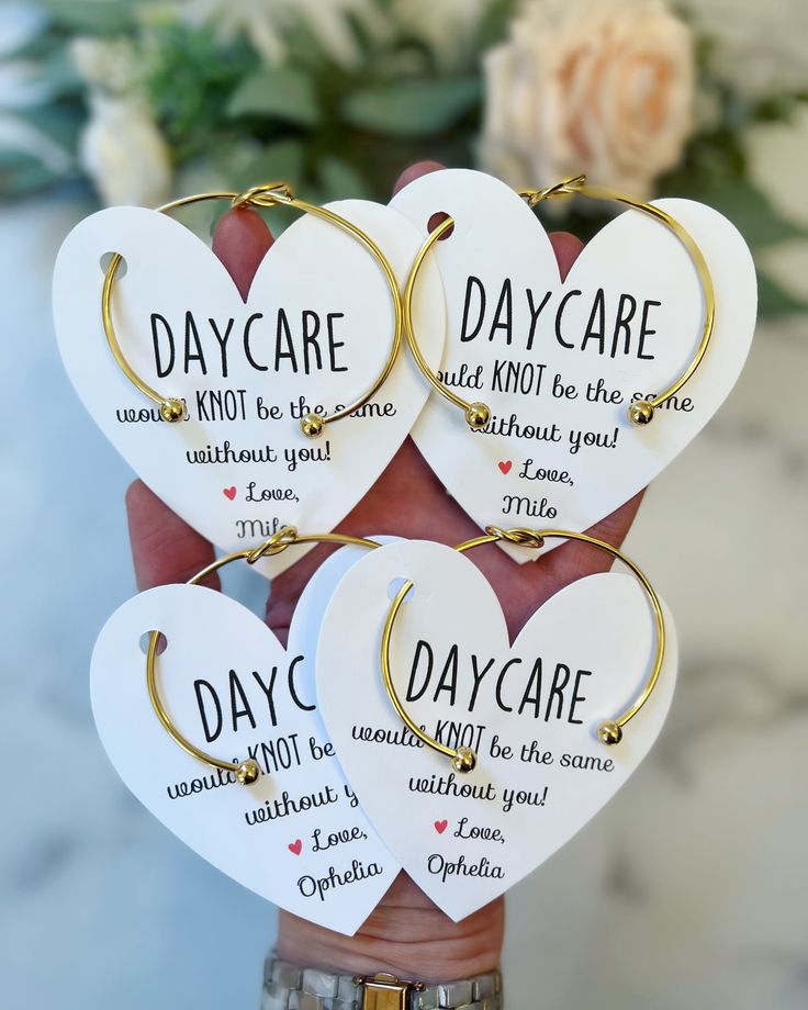 four heart shaped key chains with words on them in gold and white, hanging from a hand