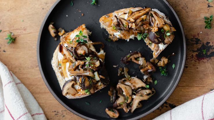 an overhead view of mushrooms and cheese on a black plate with a white towel next to it