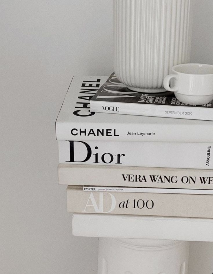 three books stacked on top of each other next to a white vase and coffee cup