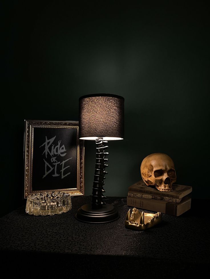 a skull sitting next to a lamp on top of a wooden table with a framed photo