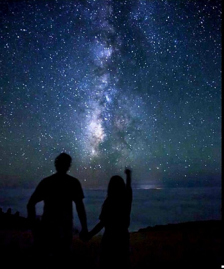 two people are standing under the stars in the sky with their hands up to each other