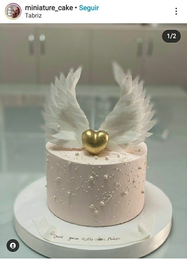 a cake with white frosting and gold decorations on the top is decorated with an angel's wing