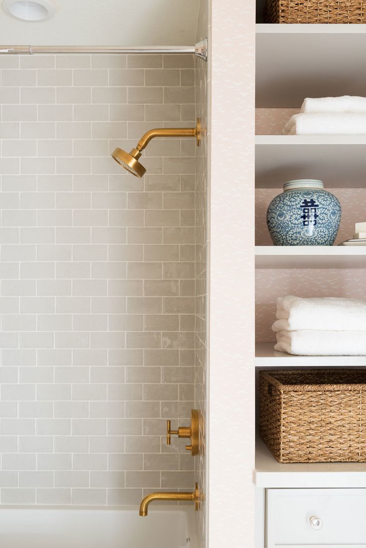 a bathroom with white tile and gold faucet, open shelve shelves