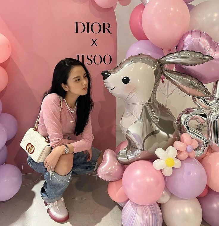 a woman sitting on the ground next to balloons and a balloon bunny statue in front of her