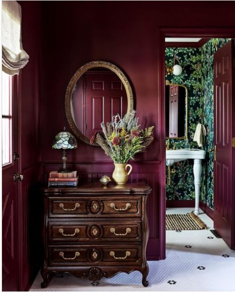 a room with red walls and a mirror on the wall next to a chest of drawers