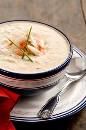 a bowl of soup on a plate with spoons and red napkin next to it