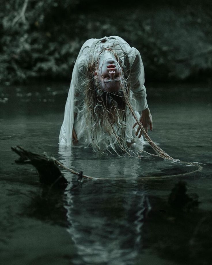 a woman with long hair is in the water and has her face covered by white cloth