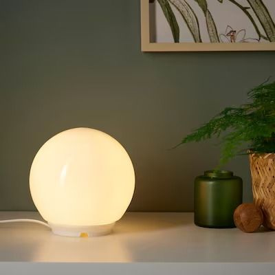 a white light sitting on top of a table next to a potted plant and vase