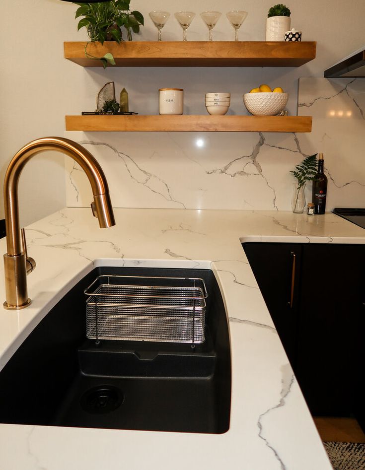 a kitchen with marble counter tops and gold faucet, black sink, and open shelving