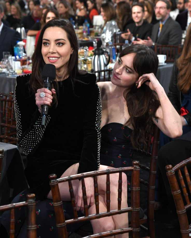 two women sitting next to each other at an event, one holding a microphone and the other