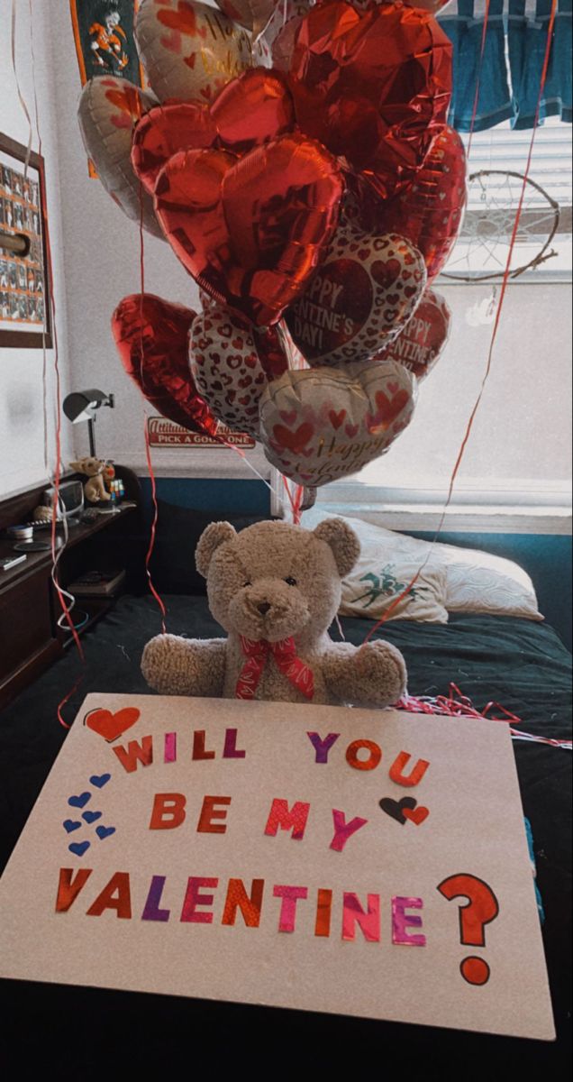 a teddy bear sitting on top of a sign that says will you be my valentine?