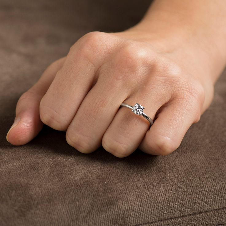 a woman's hand with a diamond ring on her left hand, sitting on a couch