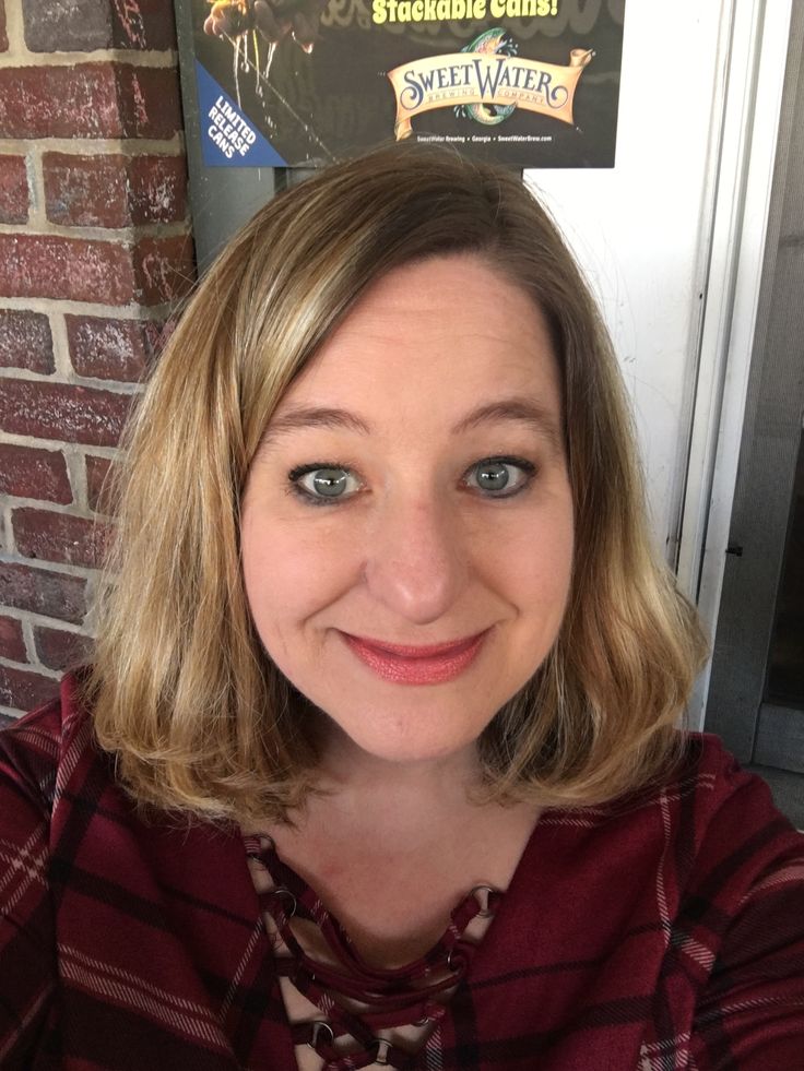 a woman with blonde hair and blue eyes smiling at the camera while standing in front of a brick wall