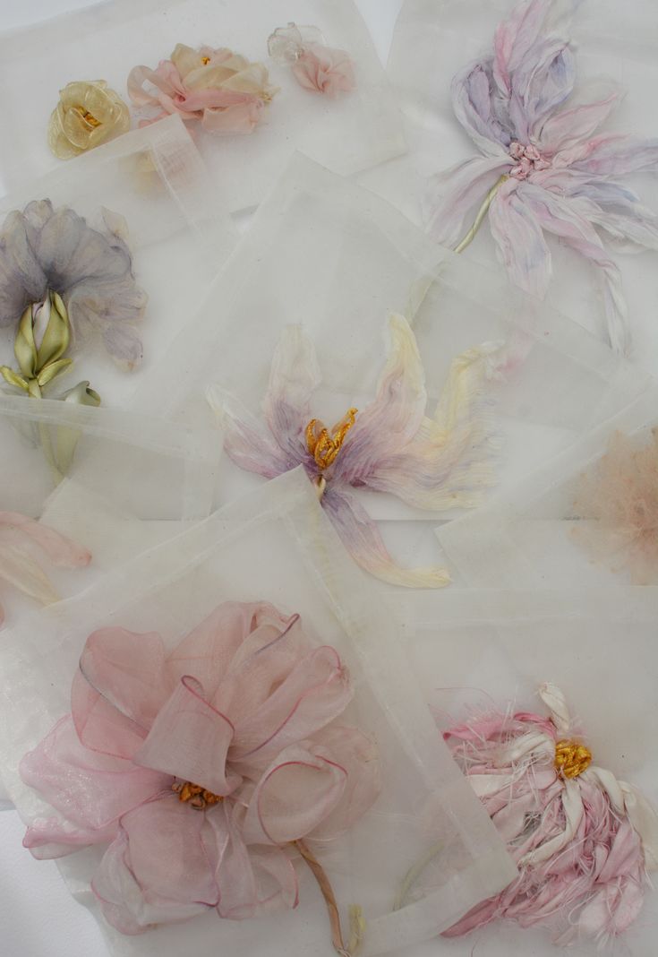 several different colored flowers sitting on top of a white surface with clear plastic bags around them