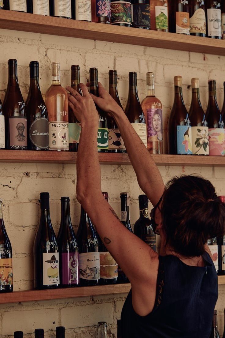 a woman is reaching up to the shelves with many bottles on it and she has her arms in the air