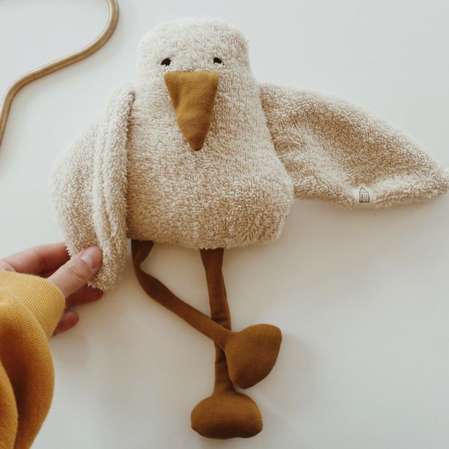 a stuffed bird is being held by someone's hand on a white table top