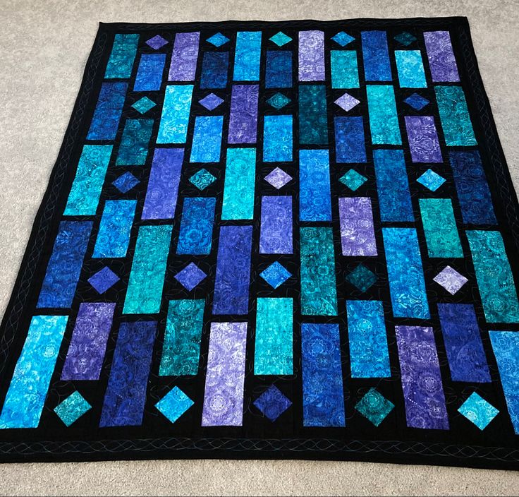 a blue and purple quilt on the floor with black backings, which are made from strips of fabric