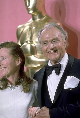 an older man and woman standing next to each other in front of a oscar statue