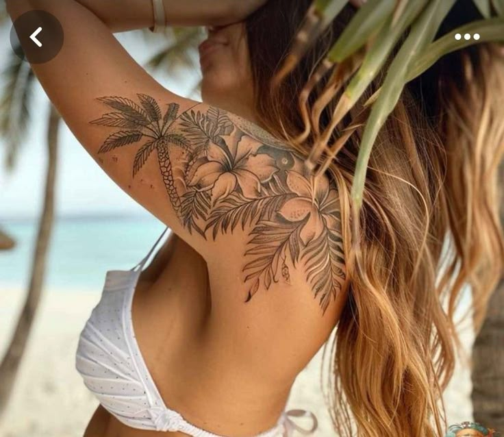 a woman with a tattoo on her back standing in front of the ocean and palm trees