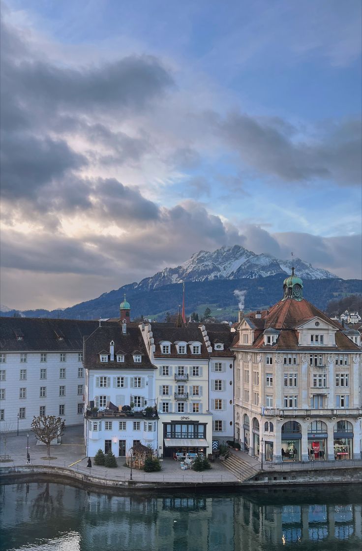 the buildings are all next to each other on the water's edge with mountains in the background