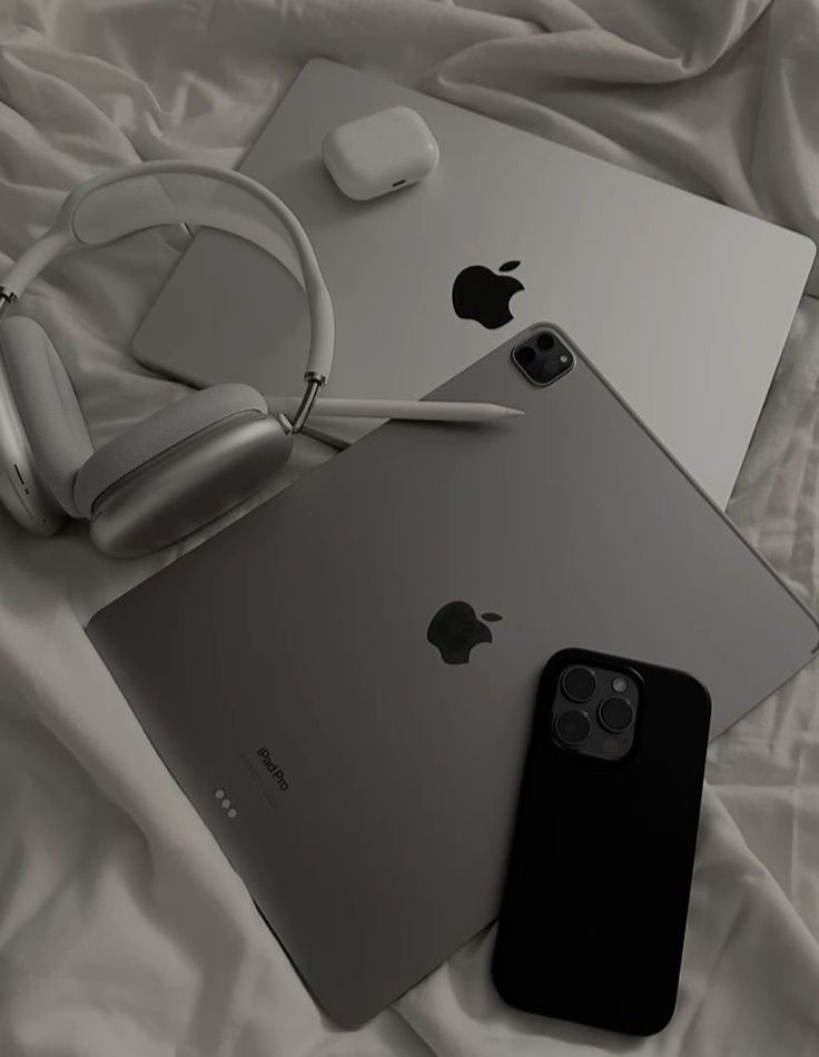 an apple phone, headphones and laptop on a white sheet with a pair of earbuds