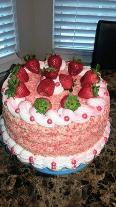 a strawberry covered cake sitting on top of a counter next to a pair of windows