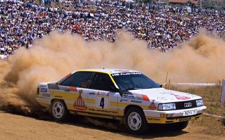 a car driving on dirt with people in the background