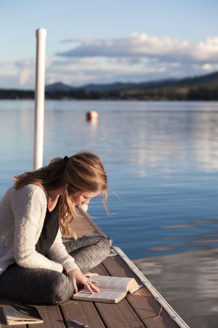 a woman sitting on a dock reading a book