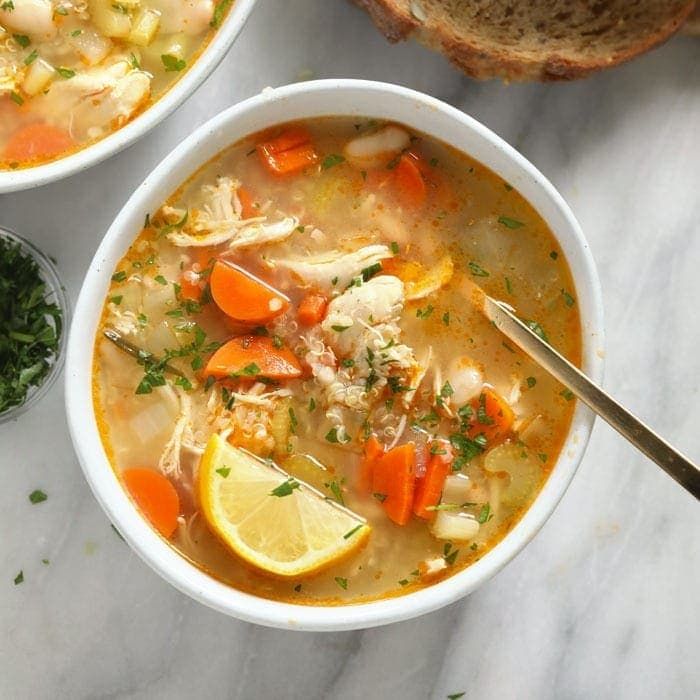 two bowls filled with chicken and vegetable soup next to some bread on a marble surface