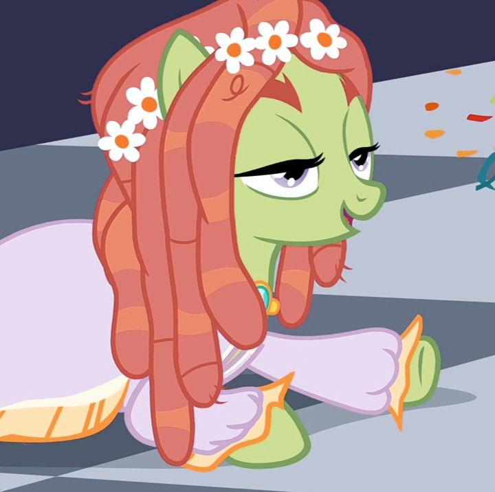 the pony is sitting on the ground with her head down and flowers in her hair