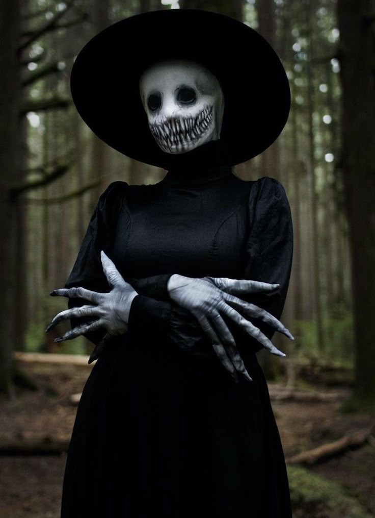 a woman dressed as a skeleton in the woods with her hands on her chest, wearing a black dress and hat