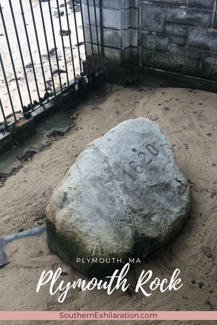 a large rock sitting in the sand next to a fence and gate with words plymouth rock written on it