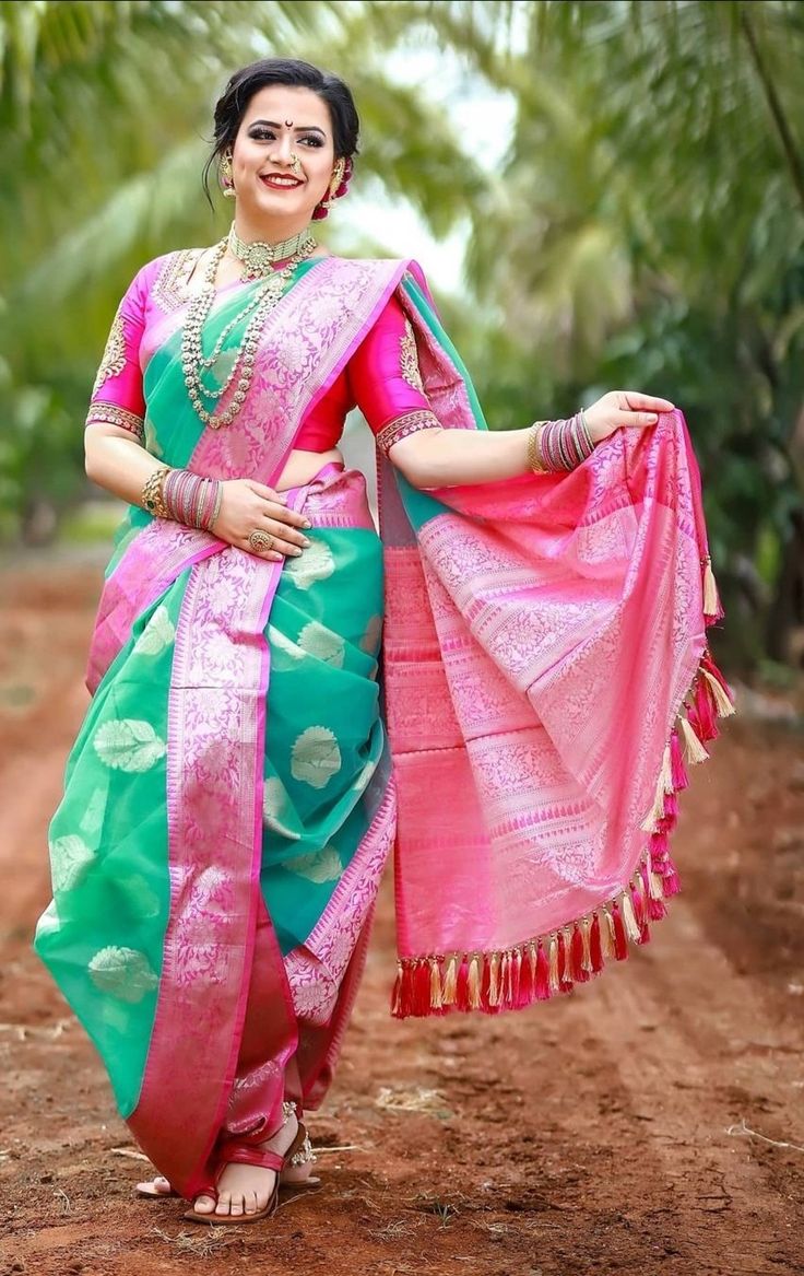 a woman in a pink and green sari is standing on the dirt road with her arms around her waist