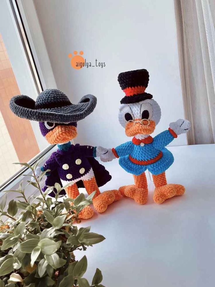 two crocheted ducks dressed in costumes, one wearing a hat and the other holding hands